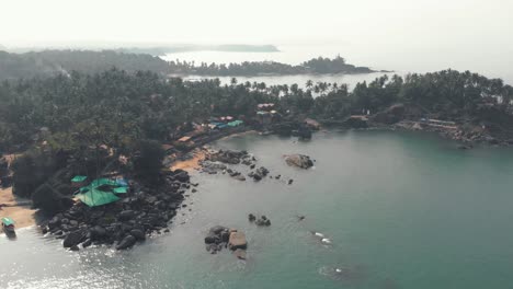 Rocky-beach-embankment-on-the-edge-of-Palolem-Beach-near-Colomb-Beach-in-Goa,-India---Aerial-slow-orbit-shot