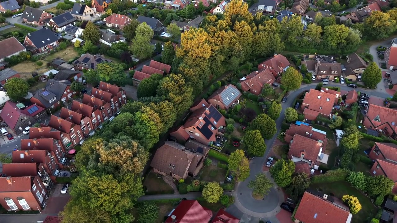 Sakin bir Alman mahallesinde, sonbahar renkli ağaçların yoğun kümesi etrafında sıralanmış kırmızı çatılı evler, kavisli bir araba yolu boyunca güneş panelleri ve park halindeki arabalar. Havadan drone ile yukarıdan aşağıya genel çekim