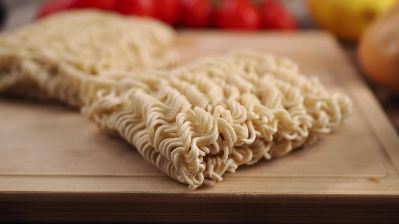 Primo piano di noodles istantanei crudi su un tagliere di legno.