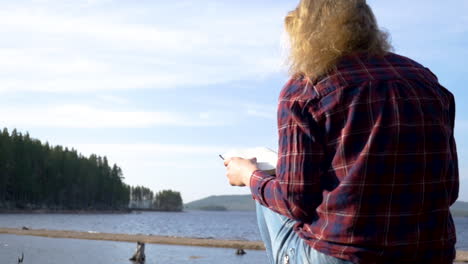 Girl-sitting-and-reading-a-book-at-a-lake-on-a-sunny-day