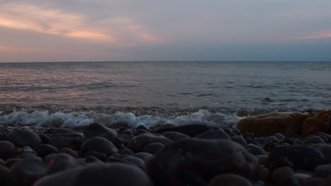 toma en ángulo bajo de las olas del océano chocando contra varias rocas y piedras en la playa durante la puesta de sol