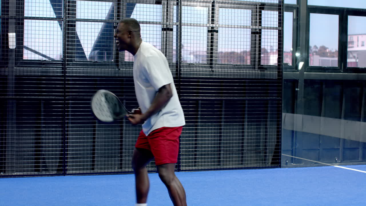 Man enjoying padel tennis game on indoor court, holding racket and smiling