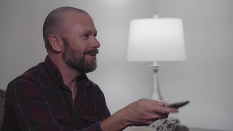 a man with a beard scans through several tv channels using a remote control