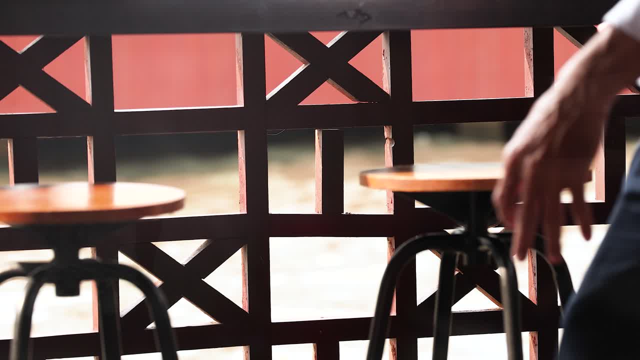 A man walks past an outdoor café in Bangkok, Thailand, with bright sunlight casting shadows on the scene