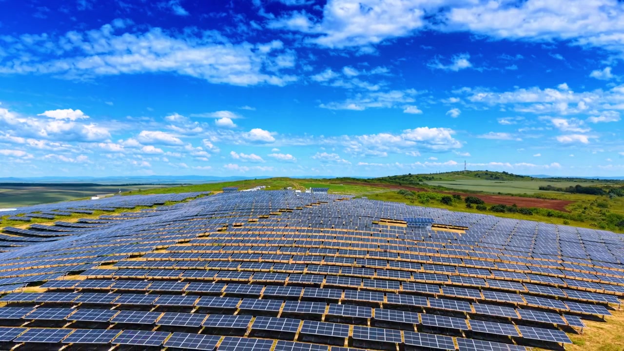 Solpaneler dækker en stor bakke under blå himmel. Panoramisk luftfoto af et massivt solcellekraftværk i et grønt landskab med skyer