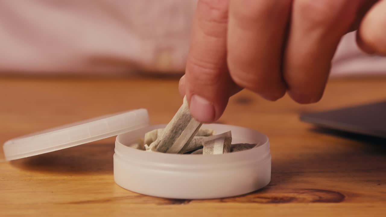 Snus nicotine tobacco close up, pack of tobacco for gum. unhealthy addiction. Man opening box with snus and taking one.