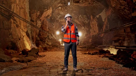 full body of asian male engineer with safety helmet talking on smartphone while standing in underground mine tunnel