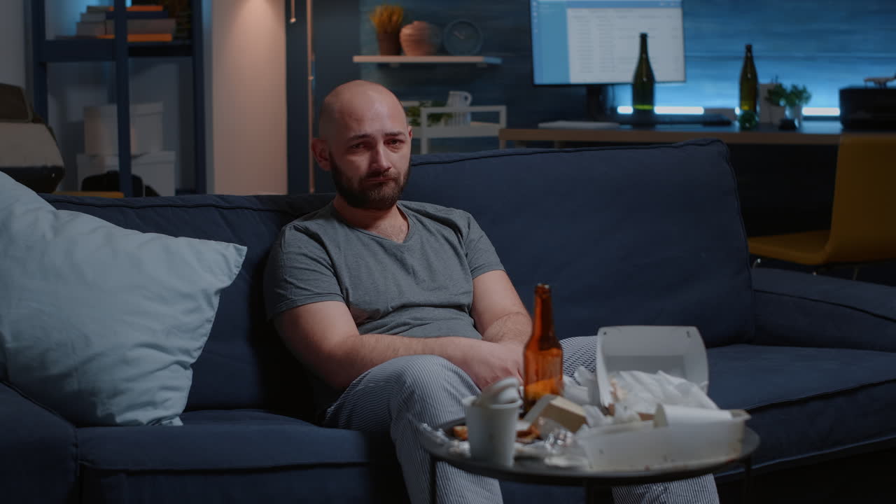 Depressed apathetic worried man sitting on sofa crying looking at camera