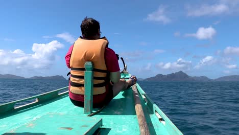 A-male-tourist-sitting-on-the-end-of-the-boat,-enjoying-the-sunlight-and-the-scenery-at-El-Nido-Palawan,-Philippines