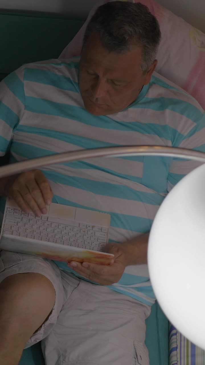 Man lying on bed typing on laptop