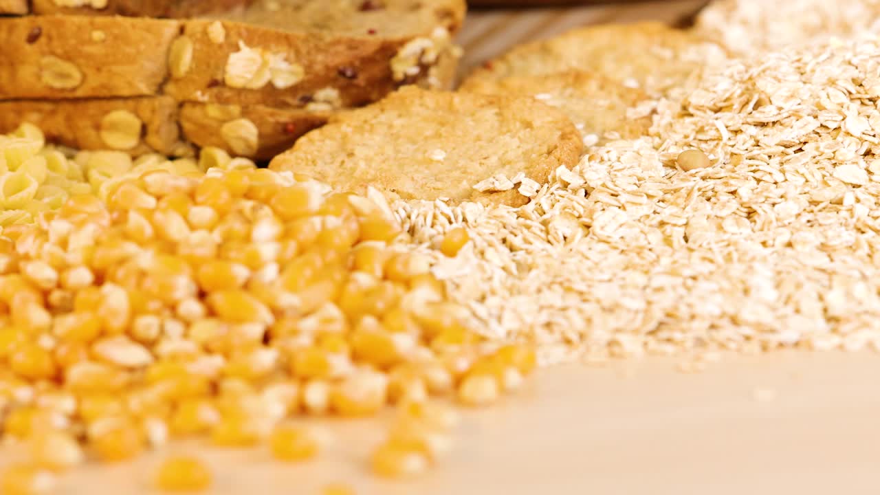 A variety of grains and pasta arranged on a wooden surface under bright lighting, highlighting textures and colors