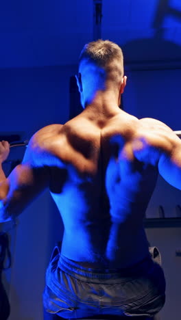 backside view of an athlete exercising. sportsman sitting and doing his workout on a simulator in the sports center. blue light. vertical video
