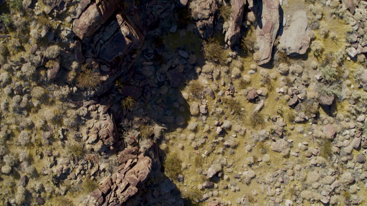 Bird’s-eye view of rugged Palm Springs mountain terrain, showcasing dramatic ridges, rocky slopes, and desert textures under a clear blue sky. A striking natural landscape from above