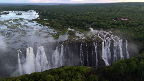 aerial view of victoria falls with powerful waterfall plunging into gorge, mist rising above lush green forest, dramatic natural wonder and iconic travel destination in africa