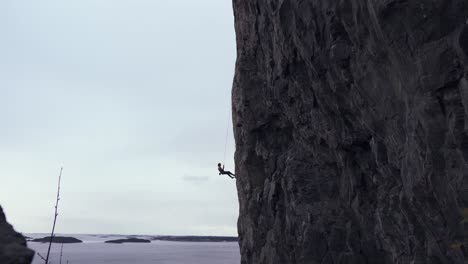 man rappelling down a vertical mountain, ocean view in background