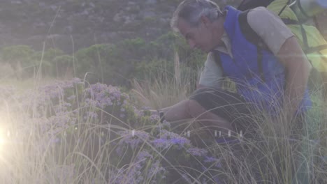 Happy-caucasian-senior-man-hiking-in-countryside-over-moving-rays-of-light