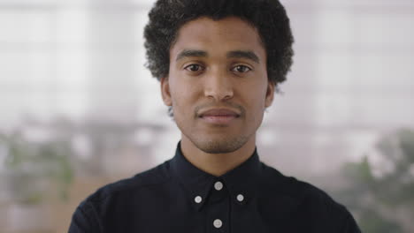 close up portrait of young confident mixed race man looking at camera smiling proud in office workspace background