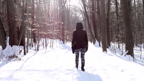 woman walking in snow in winter clothes during cold sunny day - static shot