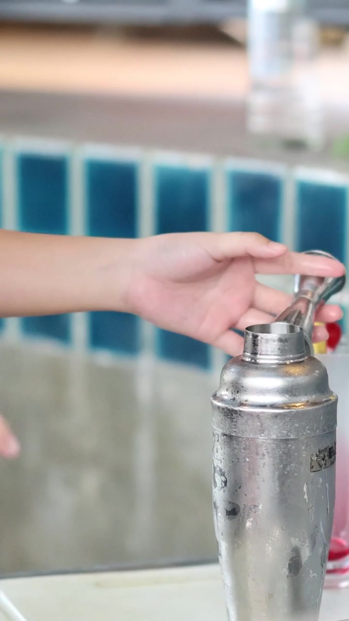 Las manos de un camarero miden líquido rojo en un jigger de metal junto a una coctelera.
