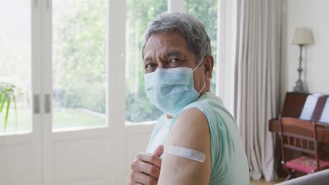 Portrait-of-senior-man-wearing-protective-face-mask-showing-covid-vaccine-bandage-on-shoulder