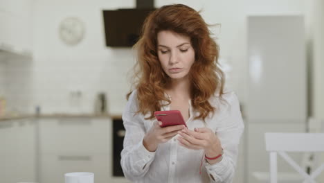 serious woman taking phone at open kitchen. young lady closing laptop at home.