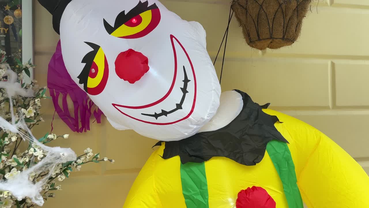 An inflatable clown decoration for Halloween featuring a menacing smile, red nose, and colorful outfit, holding a hammer with “Happy Halloween” written on it.