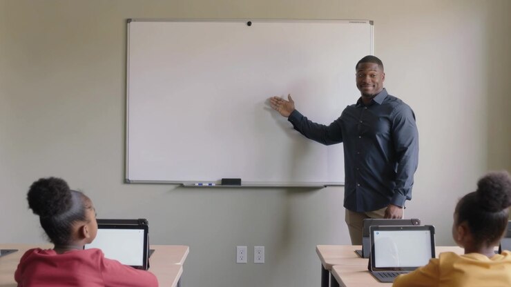 Starting lesson instructor in dark shirt gesturing at whiteboard in class, students on tablets