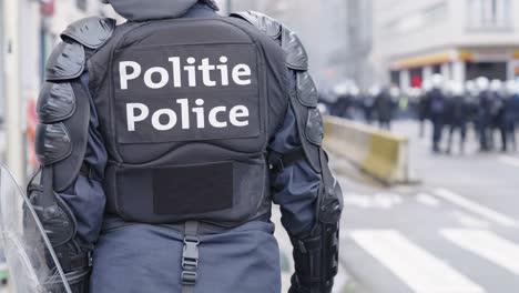 a belgian police officer in riot gear standing on an urban street awaiting orders