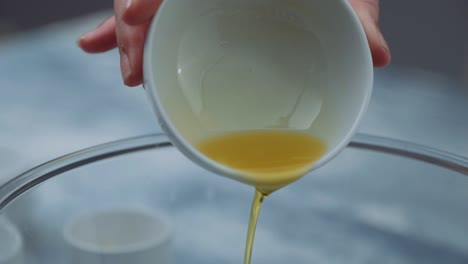 pouring olive oil from a small white ceramic bowl ramekin