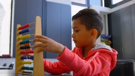 vista lateral de un escolar asiático resolviendo un problema de matemáticas con ábaco en el escritorio en un aula de la escuela 4k