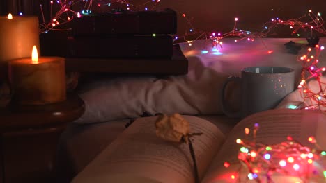 cozy background of an open book on a bed, next to a mug and surrounded by colorful christmas lights