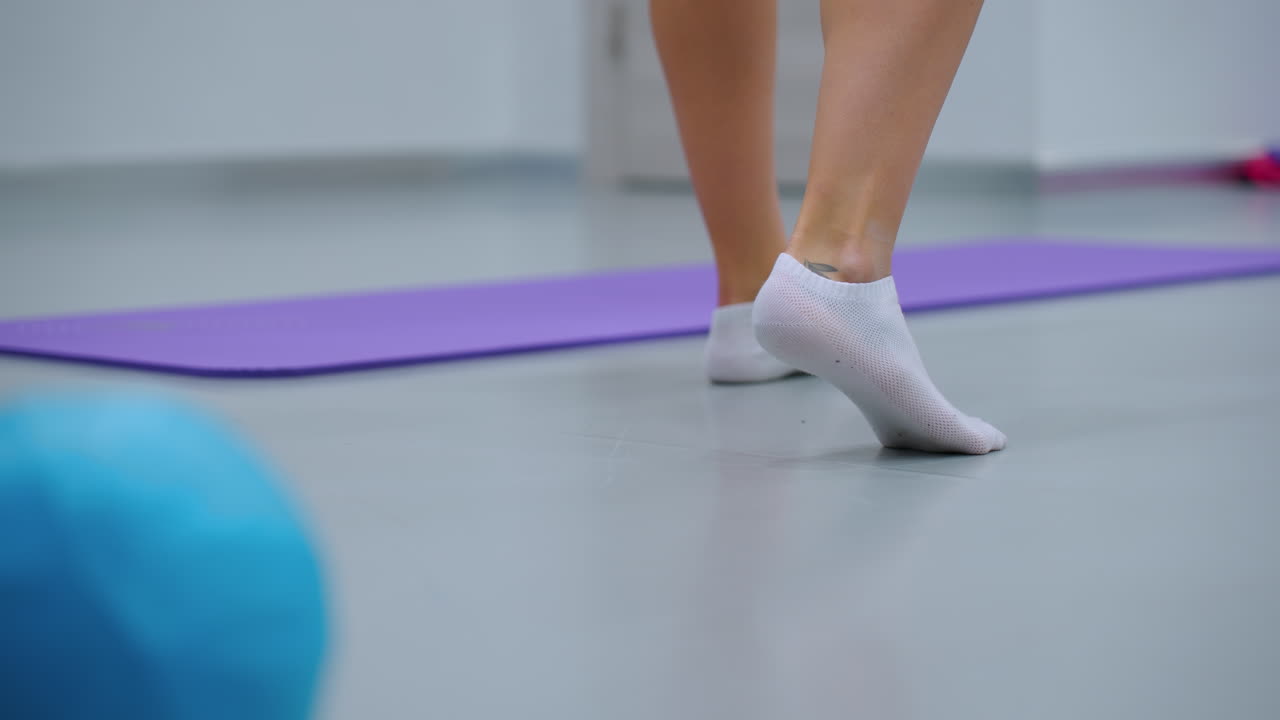 양말을 입고 한 발에 균형을 잡고 파란색 풍선 근처에 을 올리고, 바닥에 보라색 매트, 체육관 환경을 볼 수 있으며, 안정성을 포착하고, 피트니스에서 균형 훈련을합니다.