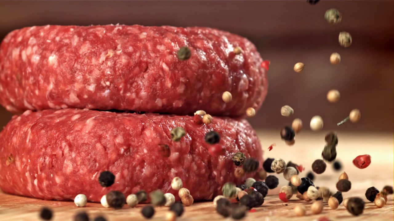 Grani di pepe che cadono su hamburger di manzo crudi