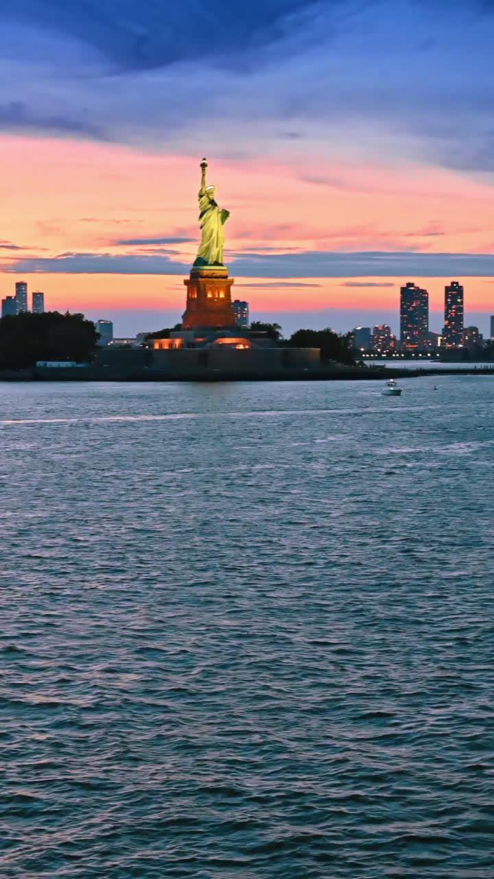 New York, USA, 8 luglio 2025: Statua della Libertà illuminata con luce gialla al tramonto. Cielo nuvoloso arancione sullo sfondo. Barca in viaggio a New York, USA. Video verticale