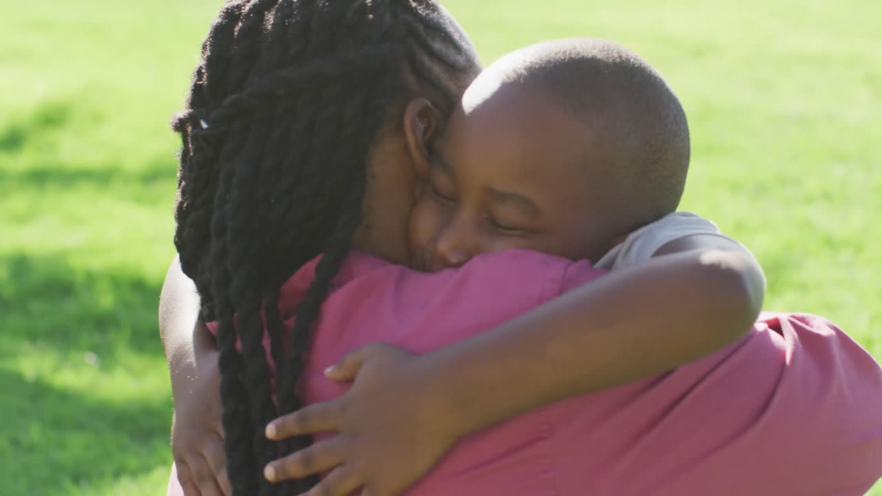 Video of happy african american father and son having picnic on grass and hugging