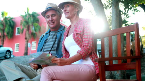 una pareja de turistas felices sentados en un banco sosteniendo un mapa