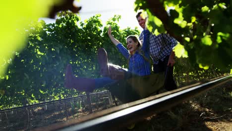 Man-carrying-woman-in-wheelbarrow-through-vineyard