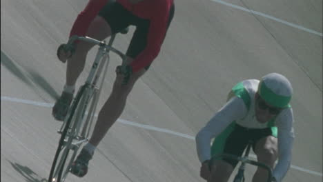 two men ride bicycles one makes gestures with his hand