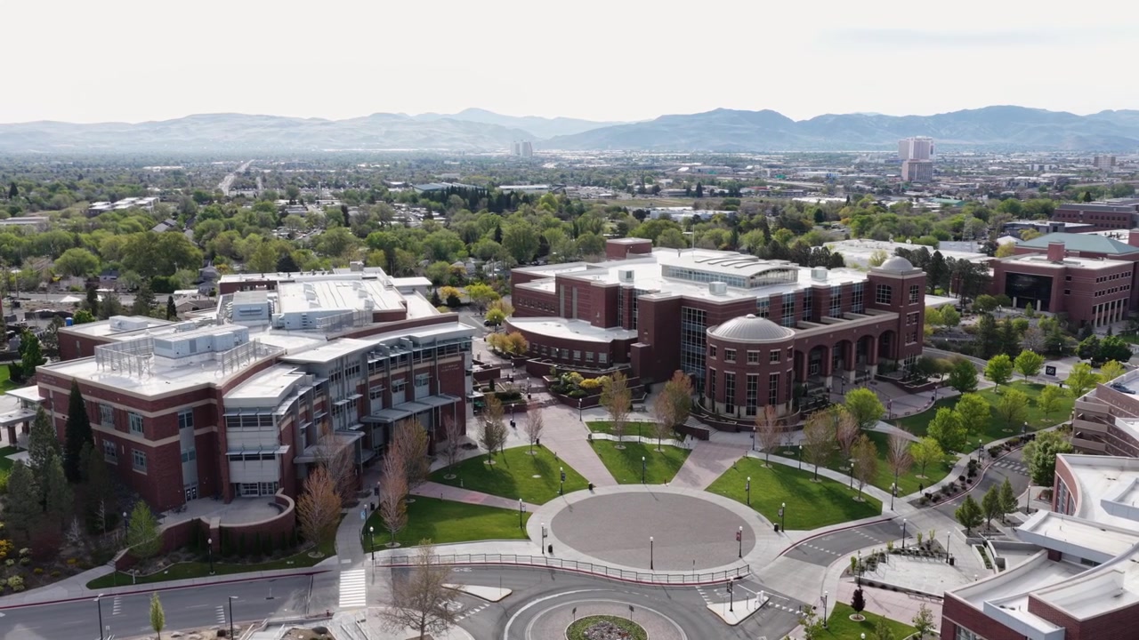 Campus universitario con edifici in mattoni rossi, facciate in vetro e una biblioteca a cupola attorno a una piazza circolare, prati verdi e sentieri alberati con una catena montuosa all'orizzonte. Nevada, USA. Veduta aerea