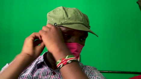 african man wearing red face mask and safari jungle hat in front of green screen