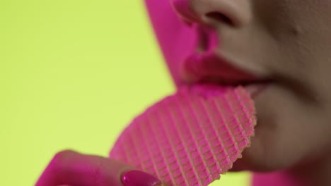 mujer comiendo un waffle crujiente en primer plano, esmalte de uñas femenino y labios de lápiz labial rojo sobre fondo amarillo