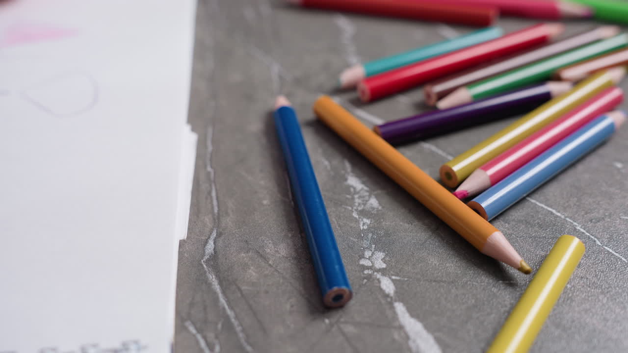 Close up of student drawing with colorful pencils scattered on gray table beside sketchbook, representing creativity, learning, imagination, playful expression through drawing activity