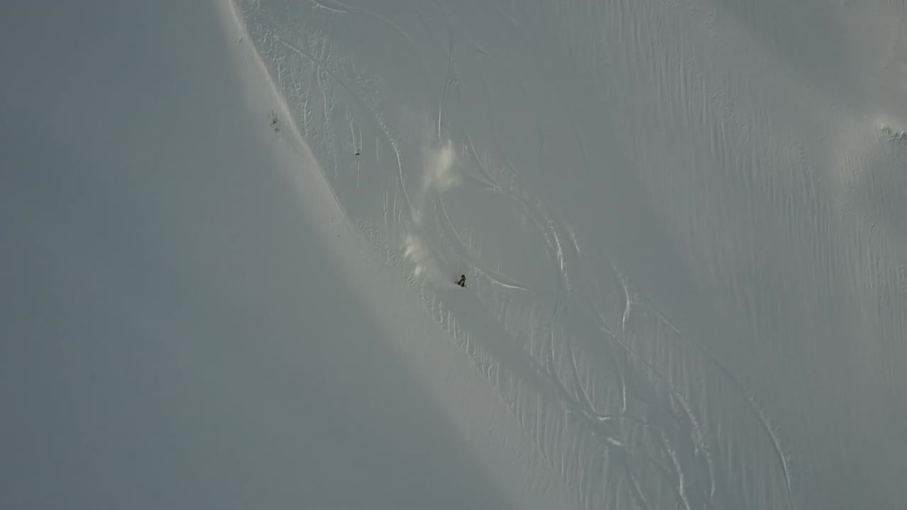 백컨트리에서 열린 파우더 슬로프를 타고 내려가는 드론 추적 스노보더