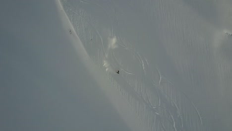 drone tracking snowboarder riding down open powder slope in backcountry