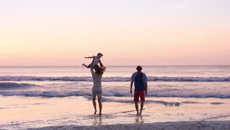 mother swinging little girl around happy family on the beach holding hands  at sunset on vacation