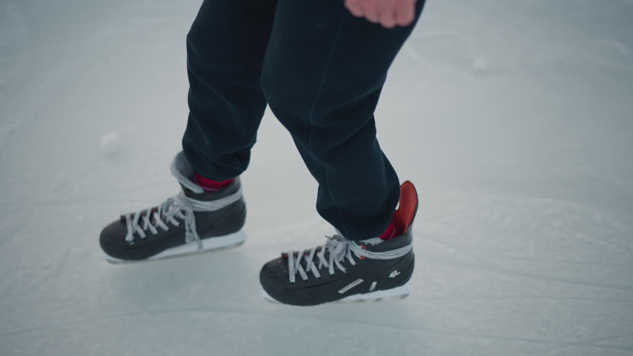 close up leg view of skater in black trousers skillfully skating across ice rink under crisp winter sunlight with visible ice markings beneath blades showcasing fluid motion and balance
