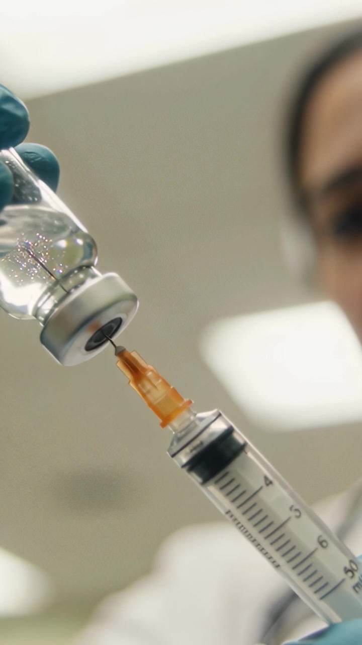 Vertical video: Gloved hand filling syringe after needle piercing vial at clinic, preparing dose