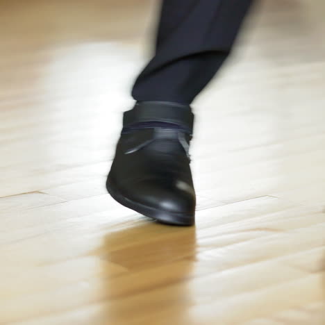 man in black leather shoes dancing on the wooden floor. male's legs in black trousers and new shoes shows some kind of dance on a parquet. close-up