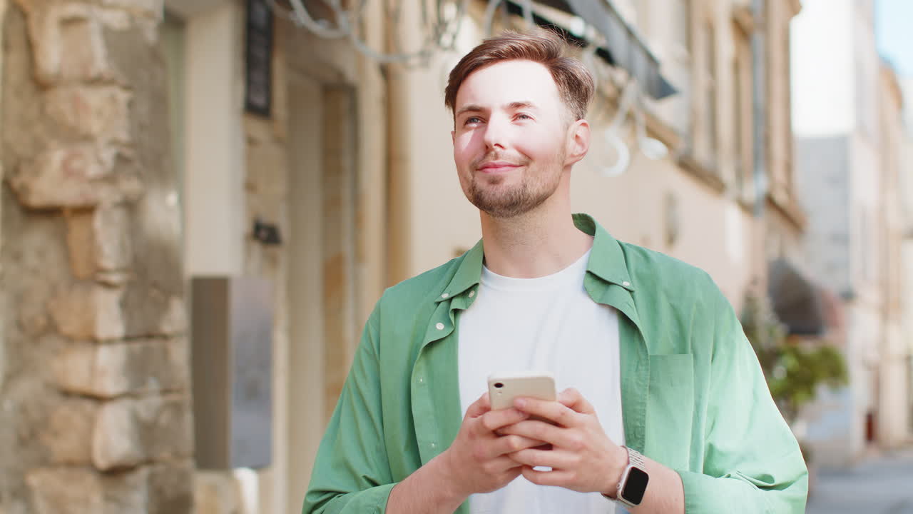 Giovane uomo utilizza lo smartphone digitando messaggi, applicazioni di social media ed email per strada.