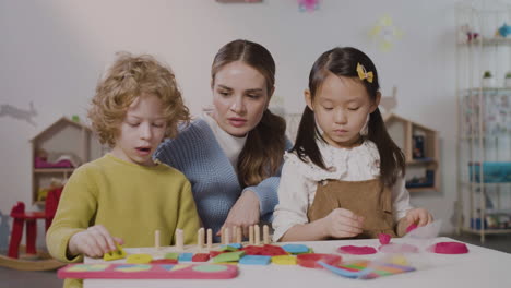 Two-pupils-in-a-Montessori-school-playing-with-shapes-stacking-and-play-dough-while-teacher-helping-them